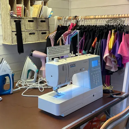 Symaskin på arbetsbord framför färgstarka scenplagg